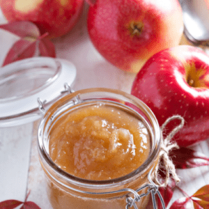 homemade apple butter in a jar surrounded by apples