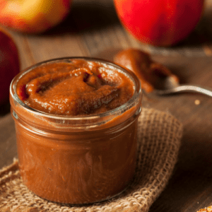 homemade apple butter in a jar on a table surrounded by apples